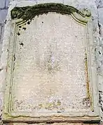 Photographie d'une pierre gravée adossée à un mur.