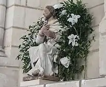 Statue montrant un apôtre assis, entourée d'une couronne de fleurs.
