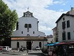 Vue d’un édifice religieux à murs blancs donnant sur une placette.