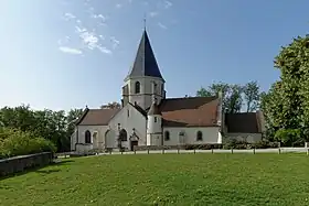 L'église vue d'une rivière en contrebas, et en partie masquée par la verdure