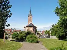 Photographie couleur de la façade d'une église en grès rose, surmontée d'un haut clocher