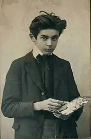 Photo noir et blanc en plan américain d'un adolescent à l'air sérieux, en costume sombre, palette à la main