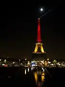 La Tour Eiffel illuminée de nuit, avec le haut de la tour rouge, le milieu jaune et le bas noir.