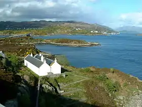 Vue d'une partie d'Eilean Bàn prise du pont de Skye avec la ville de Kyle of Lochalsh en arrière-plan.