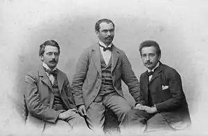 Photo en noir et blanc montrant trois hommes assis.