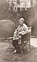 Photographie en noir et blanc d'une dame âgée assise dans un jardin.
