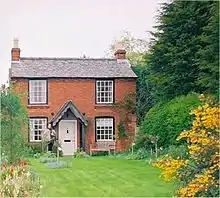 une maison de campagne en briques devant un grand jardin