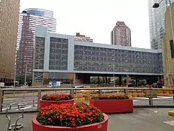 Trois bacs à fleurs avec des fleurs rouges, bâtiment en métal et verre en arrière-plan.