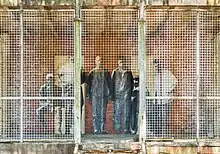 Collage d'une photographie de migrants sur un mur derrière une grille.