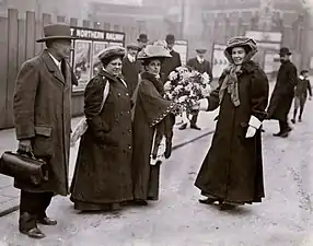 Emmeline Pethick Lawrence receiving a bouquet of flowers from Jennie Baines, Flora Drummond and Frederick Pethick Lawrence watching.