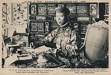 Photo ancienne représentant un homme asiatique d'environ quarante ans, en habit traditionnel, en train d'écrire à un bureau.