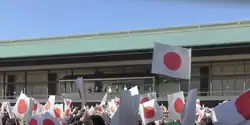 Un groupe de personnes agite des drapeaux japonais devant un palais.