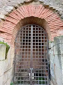 Vue d'une ouverture dont l'arc est réalisé en briques, et fermée par une grille
