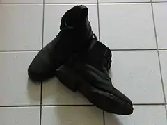 Chaussures montantes noires posées sur du carrelage.