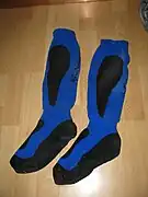 Des chaussettes bleu vif avec des bandes noires au niveau des mollets et de la plante des pieds sont posées sur un plancher.