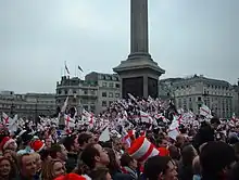 Une foule impressionnante d'Anglais avec beaucoup de petits drapeaux anglais fêtent la victoire de leur équipe sur une place par un temps couvert.