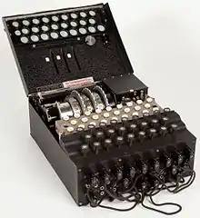 Photographie du boîtier ouvert d'une machine Enigma montrant des touches, des rotors et des câbles.