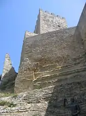 Une muraille et une tour massives, quasiment sans ouvertures, vues en contre-plongée.
