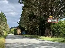  Le panneau d'entrée en agglomération au premier plan, une Citroën 2CV bleue devant un bâtiment