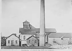 Photo noir et blanc montrant un ensemble de bâtiments industrielles dont un très haut abritant le chevalement, ce dernier dépasse surmonté d'un clocher en bois. Sur la gauche se trouve une grande cheminée.
