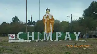 Photo en couleurs d'un panorama semi-rural avec les lettres du village Chimpay surmontées d'une grande représentation du saint