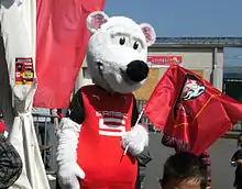 Photographie montrant une personne déguisée en hermine en peluche, avec un drapeau à la main.