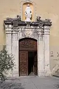 Sur le vantail gauche de la porte de cette église, le panneau supérieur présente un petit cartouche auquel est suspendu un trophée liturgique en chute