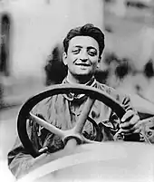 Photo d'Enzo Ferrari, souriant, derrière le volant d'une voiture.