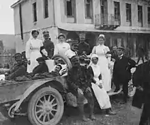 Photographie en noir et blanc montrant une groupe d'infirmières et de soldats posant autour d'une voiture transportant des blessés.