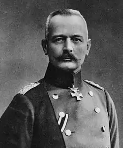 portrait photographié en noir et blanc d'un homme en tenue militaire et aux cheveux courts blancs portant une moustache