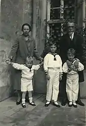 Devant une fenêtre couverte d'une treille, un couple d'âge mûr pose avec ses trois petits-fils revêtus de costumes de marin.