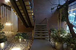 Escaliers du hall d'entrée de la résidence Vincennes, installation de Walter Leblanc à gauche, aménagement de plantes de Jean Delogne à droite, escaliers en béton, dalle béton, garde-corps en bois teck, galet blancs au sol