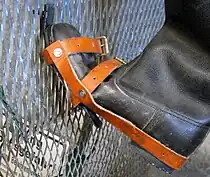 Vue rapprochée d'une botte ayant été modifiée pour recevoir des crampons montrée sur une section de clôture pour représenter son utilisation.