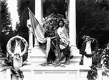 Scène extraite du film représentant une femme en toge blanche levant le bras gauche et tenant dans sa main droite un drapeau colombien, sur un monument érigé en l'honneur du Général Uribe Uribe.