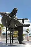 Photographie d'une statue de guitariste assis croisant ses jambes et tenant sa guitare en mains.