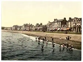 Ancienne photographie colorisée d'une plage bordée de maisonnettes.
