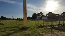 Terrain de football en herbe entouré de tribunes basses vétustes.