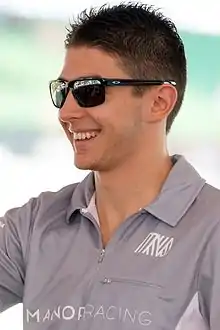 Photographie d'un homme brun, souriant, vu de trois-quarts, en gros plan, avec des lunettes de soleil.