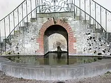 Photographie d'une source s'écoulant dans un bassin sous un double escalier.