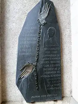 Photographie en couleurs d'une plaque d'ardoise représentant un visage, des mains enchaînées et un texte.