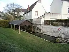 Photographie d'une bassin rectangulaire rempli d'eau et protégé par un toit, le tout appuyé à un haut mur.