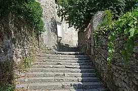 Photographie en couleurs d'un escalier extérieur en pierre entre deux hauts murs.