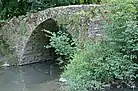 Photographie en couleurs de l'arche d'un pont en pierre au-dessus d'un cours d'eau.
