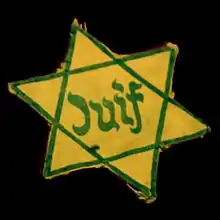 Photo sur fond noir d'une étoile de David jaune dont les deux triangles et l'inscription « Juif » sont tracés en vert foncé