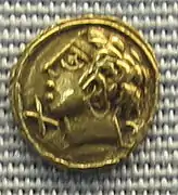 Monnaie en or sur laquelle est représentée une tête d'un homme avec des cheveux bouclés.