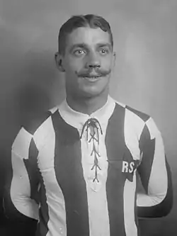 Photographie en noir et blanc d'un joueur de football avec un maillot rayé, portant la moustache.