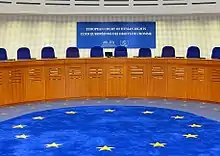 Photographie d'une salle, avec sièges bleus et logo européen sur le sol