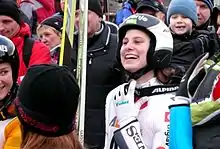 Eva Logar arborant un large sourire, avec son casque sur la tête, au milieu d'autres gens réjouis