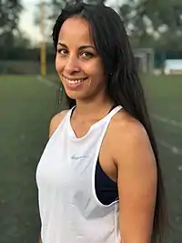 photo en couleur d'une jeune femme aux cheveux noirs, souriante, en tenue sportive.
