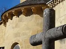 Photo du détail d'un bâtiment religieux, au premier plan le haut d'une croix, à l'arrière une tour avec des gargouilles.
